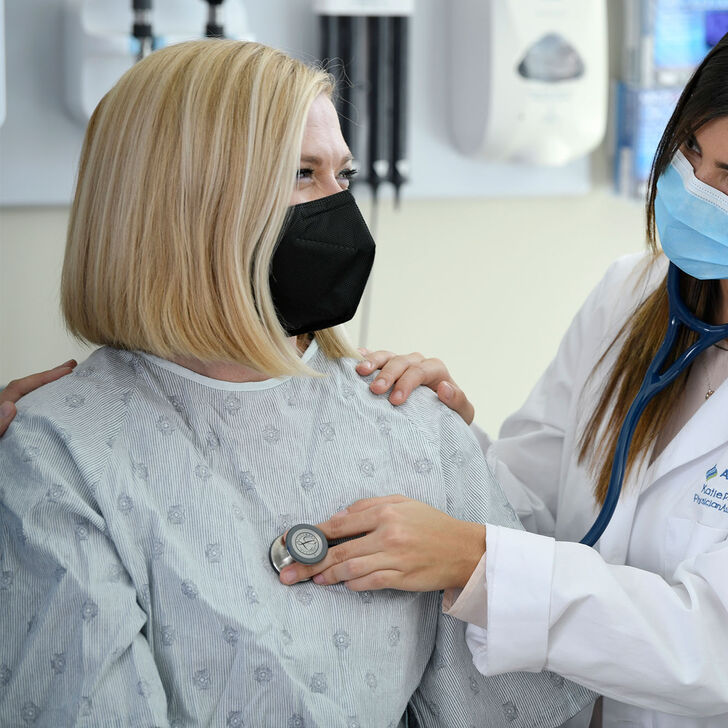A female physician assistant student using a stethoscope on a patient